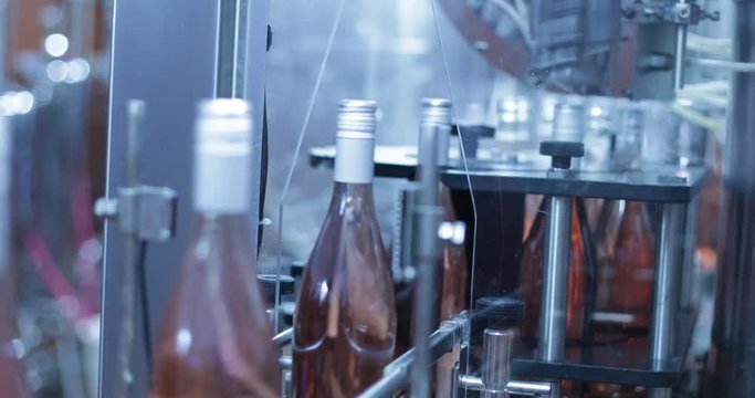 Automatic wine bottle closing machine. Detail of glass bottles being sealed with grey capsules. Efficient quick system. Camera stays still. Beverage industry process.