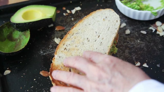 A woman cuts a peanut butter and avocado sandwich into thirds, and stacks the pieces