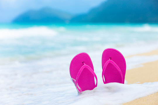 Pair of slippers on a white sandy beach. Beach vacation background.