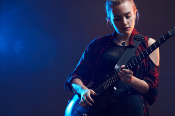 Obraz premium Blonde woman play guitar on stage, red, blue light dark scene
