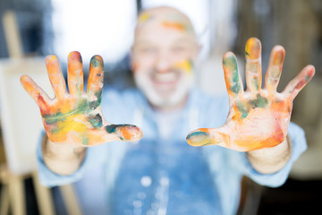 Professional painter showing his palms all in paints after working in studio of arts