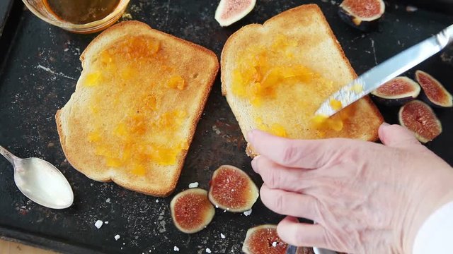 A woman adds peach jam and figs to toast slices