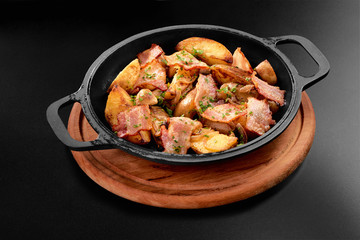 American potatoes with salt pepper parsley and cumin fried bacon in roasted black pan on wooden on black background