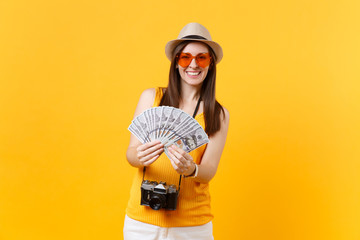 Tourist woman in summer casual clothes, hat holding bundle lots of dollars, cash money isolated on yellow orange background. Female traveling abroad to travel on weekends getaway. Air flight concept.