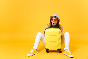 Traveler tourist woman in summer casual clothes, hat sit with suitcase isolated on yellow orange background. Female passenger traveling abroad to travel on weekends getaway. Air flight journey concept