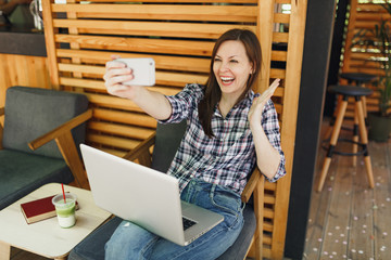 Woman in wooden outdoors street summer coffee shop sitting with laptop pc computer, doing selfie...