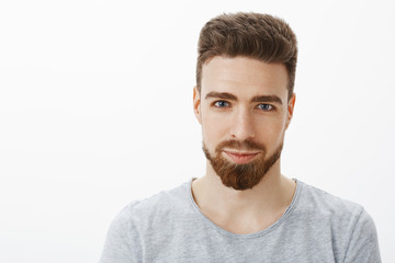 Obraz premium Waist-up shot of handsome sensual and confident young man with beard, moustache and blue eyes smiling looking sincere and self-assured at camera as with delighted smile against gray background