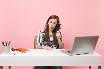 Young Curious woman scrutinizing looking through magnifying glass on pc laptop while sit work on...