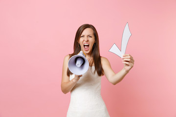 Angry bride woman in wedding dress screaming in megaphone holding check mark isolated on pink pastel background. Wedding to do list. Organization of celebration concept. Copy space for advertisement.