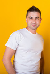 Obraz premium Handsome, cheerful, positive guy in jeans and a white T-shirt on a yellow background