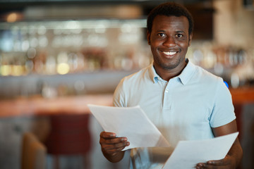 Young financier with toothy smile looking at camera while working with papers