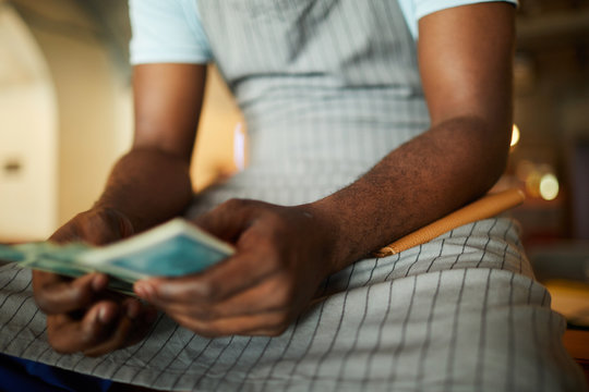 Young waiter in apron counting his earned tips at the end of working day