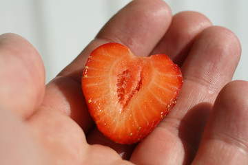 A heart shape slice of a strawberry is in hand.