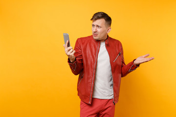 Portrait vogue upset sad young man 25-30 years in red leather jacket t-shirt talk on cellphone isolated on bright trending yellow background. People sincere emotions lifestyle concept Advertising area