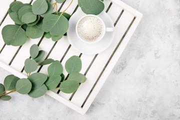 Cup of coffee on white wooden serving tray and eucalyptus branch. Flat lay, top view