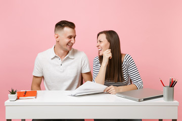 Two young laughing business woman man colleagues sit work at white desk with contemporary laptop...
