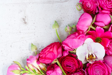 Floral composition - border made of fresh ranunculus and orchid flowers on white wooden background. Flat lay, top view, copy space