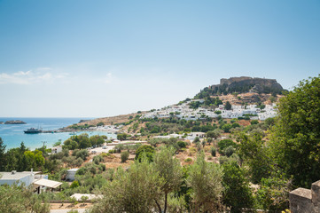 Fototapeta na wymiar Distant view at Lindos Town and Castle with ancient ruins of the Acropolis on sunny warm day. Island of Rhodes, Greece.