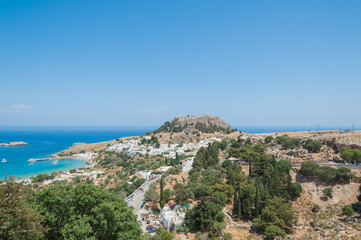 Naklejka na ściany i meble Distant view at Lindos Town and Castle with ancient ruins of the Acropolis on sunny warm day. Island of Rhodes, Greece.
