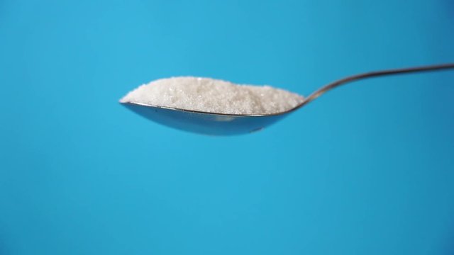 Studio video of a metal spoon pouring sugar isolated on a blue background in cooking sweet sugar addiction unhealthy diet overweight and obesity concept