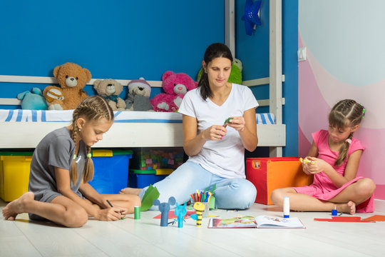 Mom and daughters sitting on the floor in the nursery make figurines for finger theater