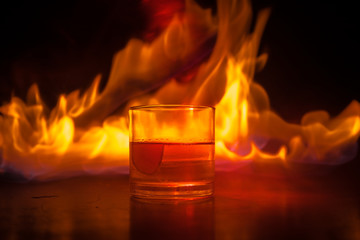 Whiskey in fire concept. Glass of whiskey and ice on wooden surface with color light and fog on background. Close up.