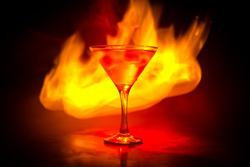 Martini in fire concept. Glass of famous cocktail Martini burning in fire at dark toned foggy background.