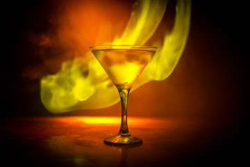 Martini in fire concept. Glass of famous cocktail Martini burning in fire at dark toned foggy background.