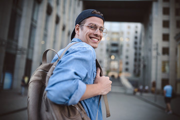 Cheerful young man with backpack enjoying walk the city