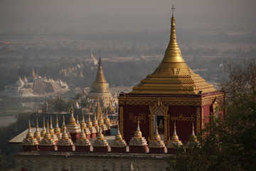 View from Sagaying hill towards a buddhist red pagoda with golden roof dome appearing behind a tree...