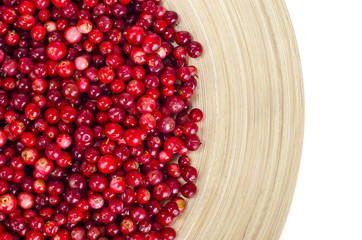 Wooden plate with red bilberry berries on white background