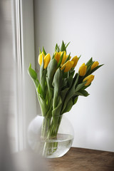 A bouquet of yellow tulips in a vase on the windowsill. A gift t