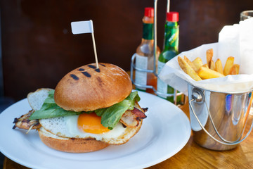 Prepare delicious burger with fried egg lettuce and grilled chicken placed on a table in white plate with fries golden potato