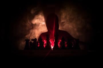 Man playing chess. Scary blurred silhouette of a person at the chessboard with chess figures. Dark toned foggy background.