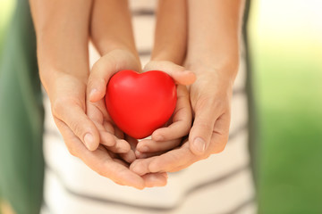 Adult and child hands holding heart on blurred background, closeup. Family concept