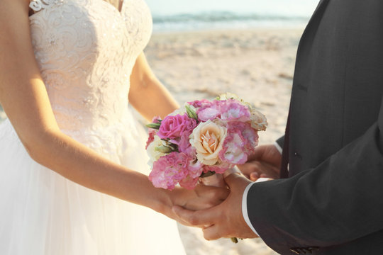 Close up view of wedding couple holding bouquet on beach