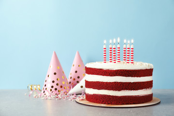 Delicious homemade red velvet cake with candles on table against color background. Space for text