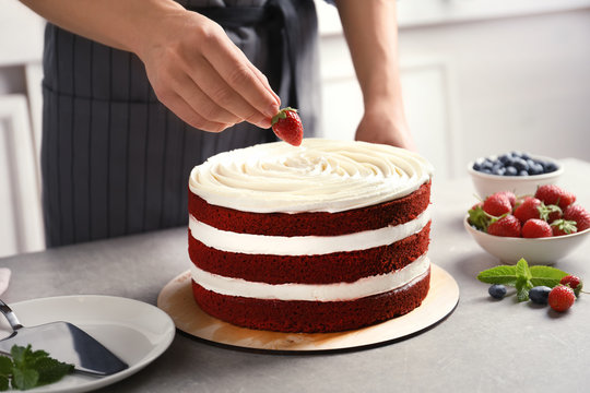 Woman decorating delicious homemade red velvet cake with strawberry at table