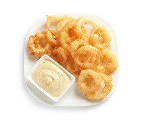 Plate with delicious crispy onion rings and sauce on white background, top view