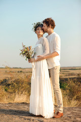 Happy newlyweds with beautiful field bouquet outdoors