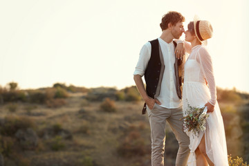 Happy newlyweds with beautiful field bouquet standing on rock outdoors