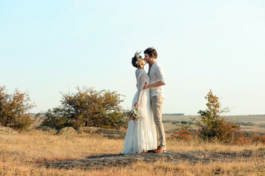 Happy newlyweds with beautiful field bouquet outdoors
