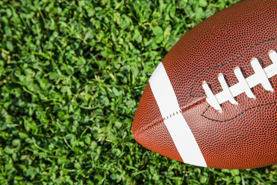 Ball for American football on fresh green field grass, top view. Space for text