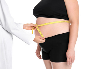 Doctor measuring fat woman's waist on white background, closeup. Weight loss