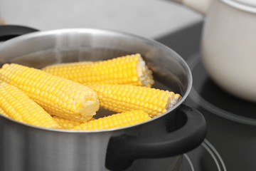 Stewpot with water and corn cobs on stove, closeup