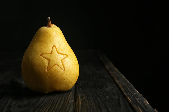 Ripe pear with carved star on wooden table against dark background. Space for text
