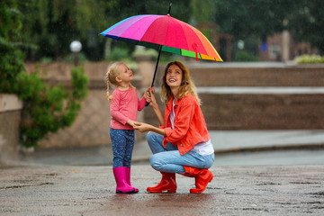 Happy mother and daughter with bright umbrella under rain outdoors