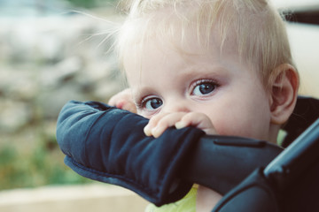 Adorable blonde baby peeking out of the stroller