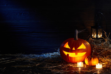 Carved pumpkin or jack-o-lantern in dark barn, Halloween holiday celebration concept