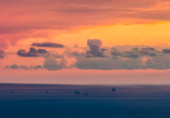 floating in the distance to the sun in the sunset sailing ships